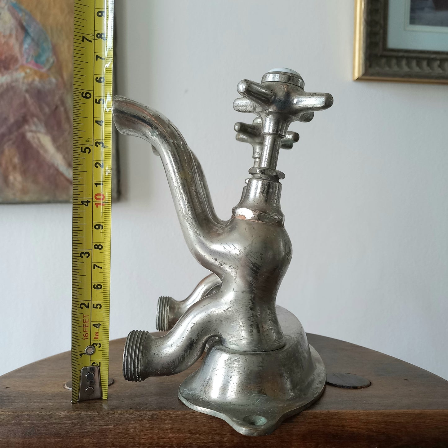 Close-up of a vintage metal faucet on a wooden background with a measuring tape showing its dimensions against a plain background