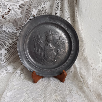 A small French vintage or antique embossed pewter plate with coat of arms depicting armor.