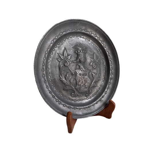 A small French vintage or antique embossed pewter plate with coat of arms depicting armor.