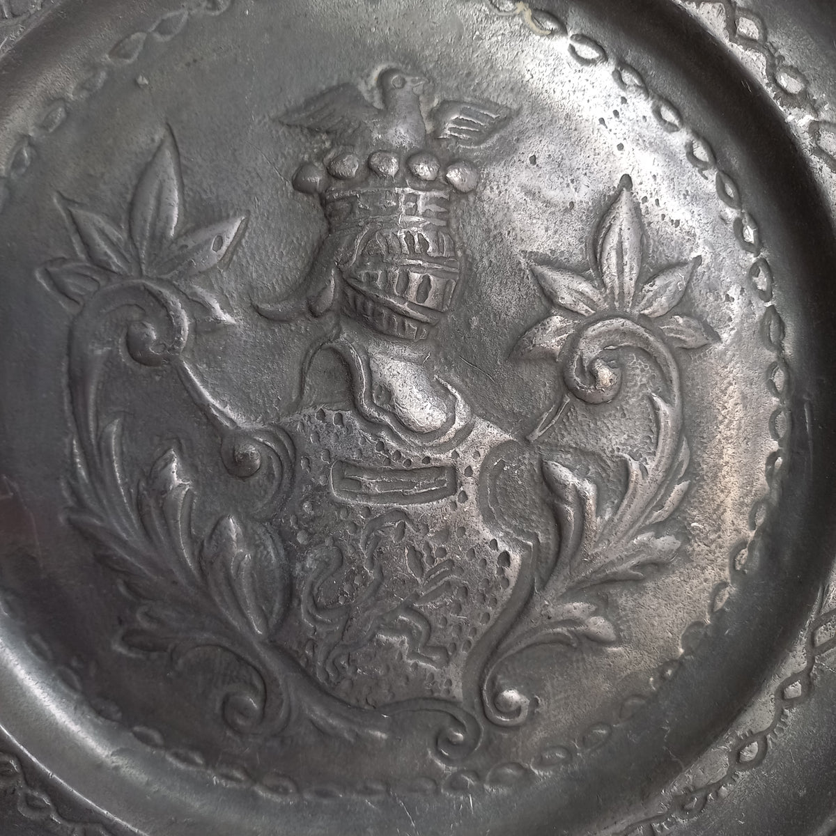 A small French vintage or antique embossed pewter plate with coat of arms depicting armor.
