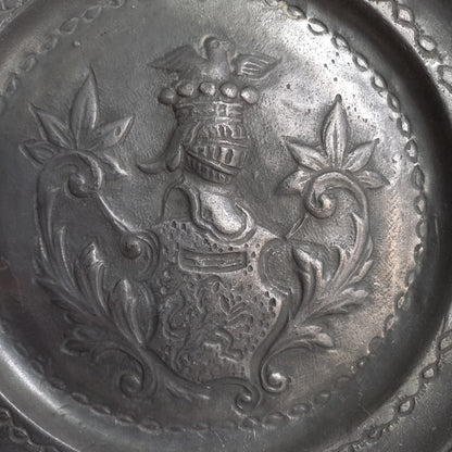A small French vintage or antique embossed pewter plate with coat of arms depicting armor.