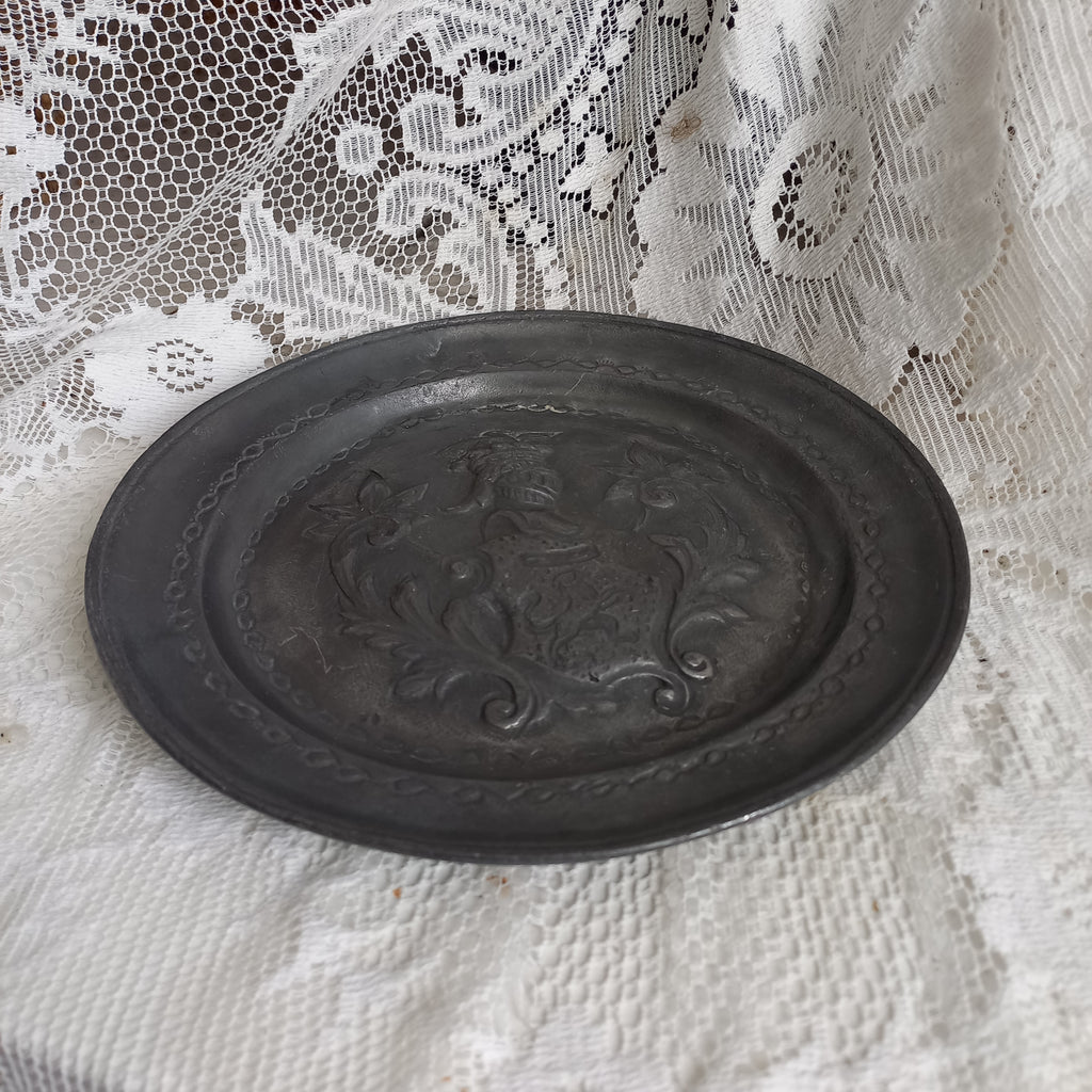 A small French vintage or antique embossed pewter plate with coat of arms depicting armor.