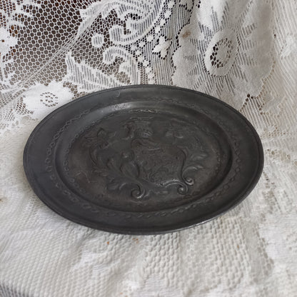 A small French vintage or antique embossed pewter plate with coat of arms depicting armor.