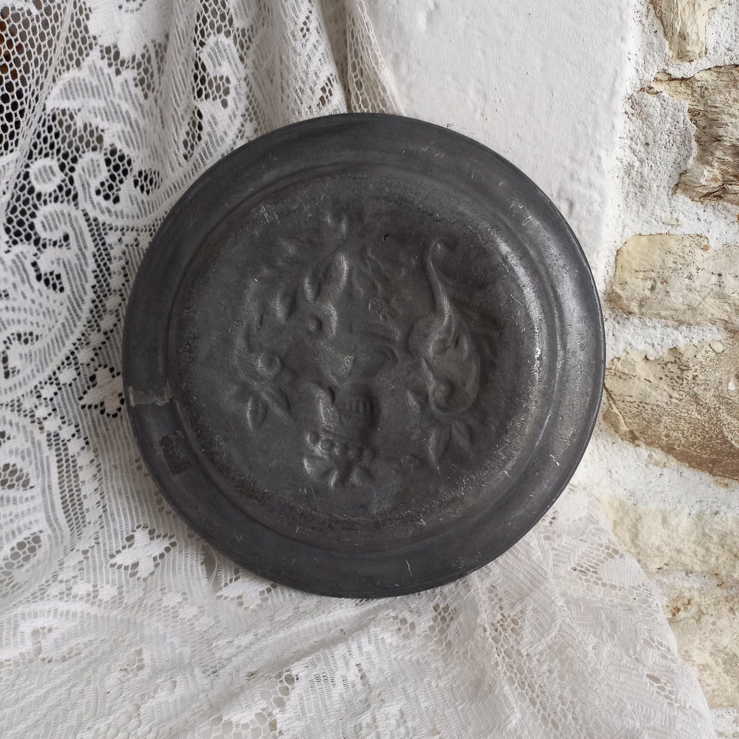 A small French vintage or antique embossed pewter plate with coat of arms depicting armor.