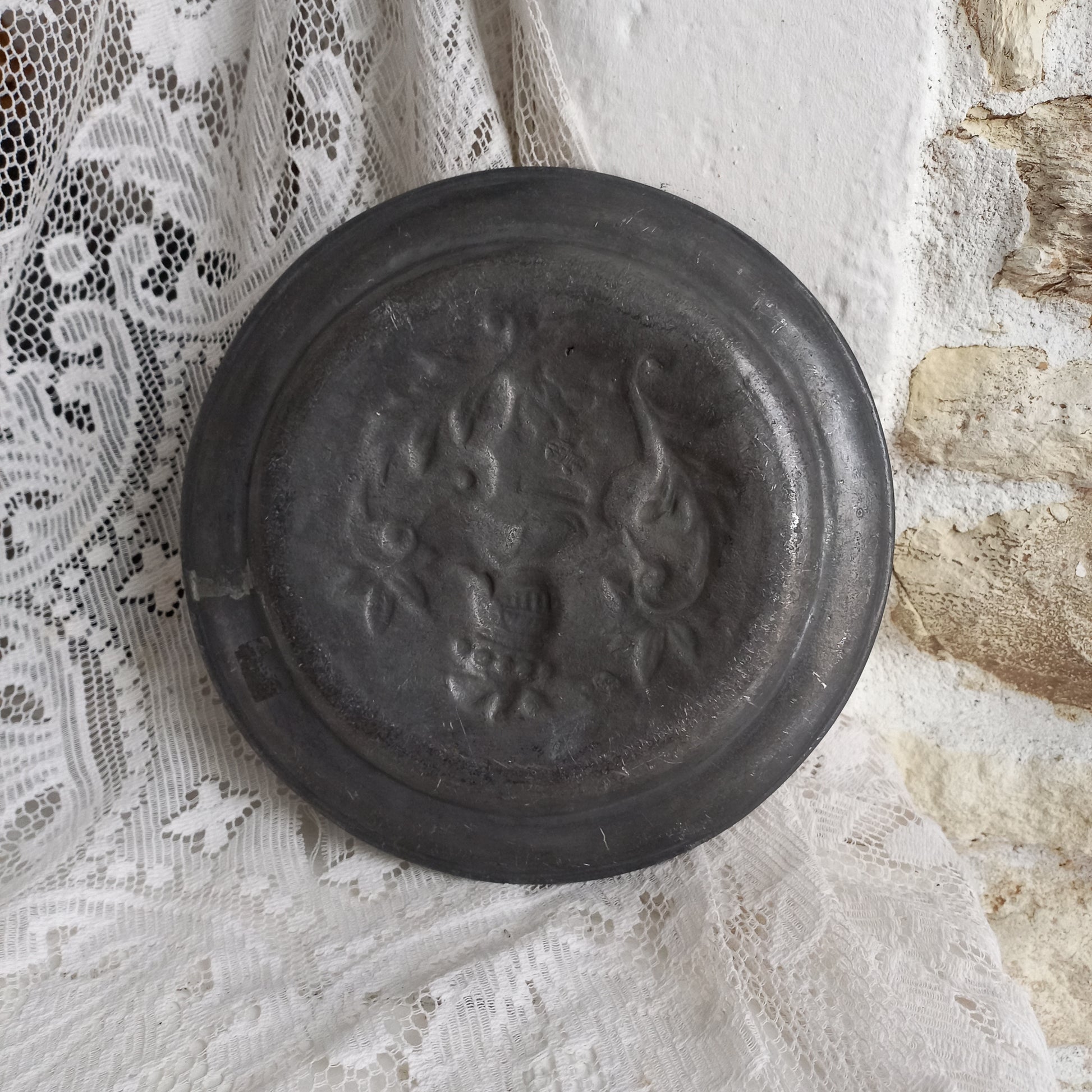 A small French vintage or antique embossed pewter plate with coat of arms depicting armor.