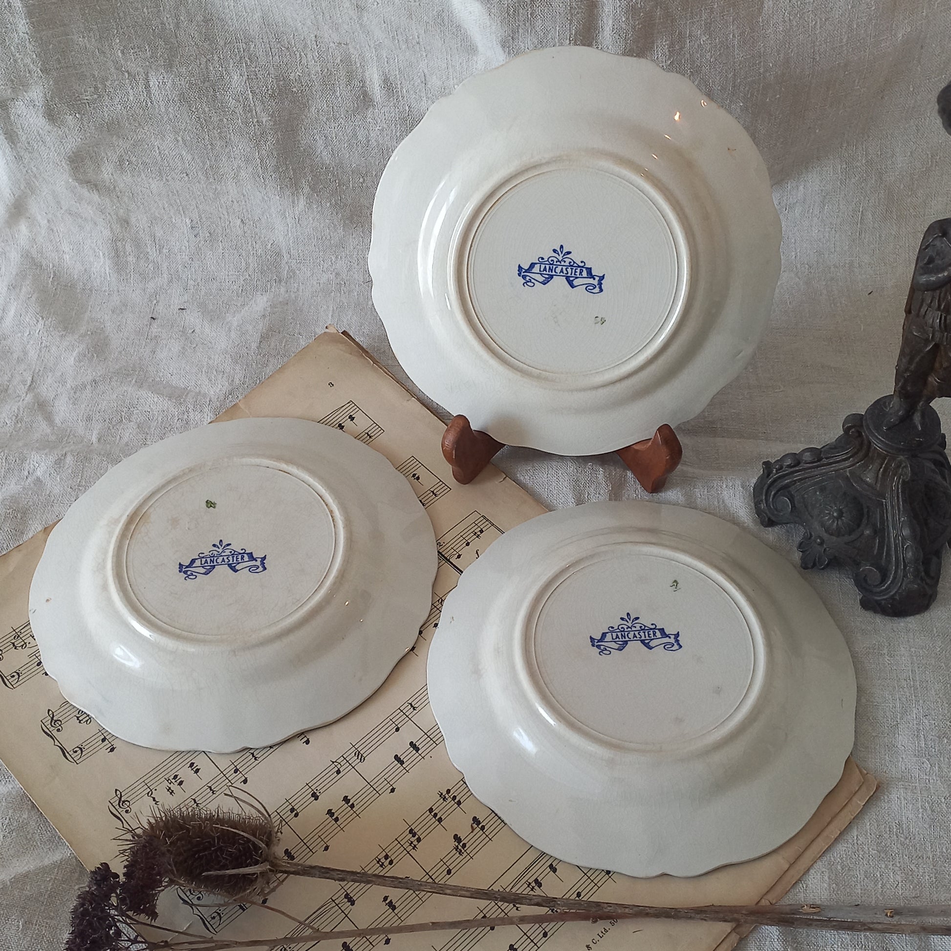Three white plates with blue designs on a surface with sheet music and decorative items.