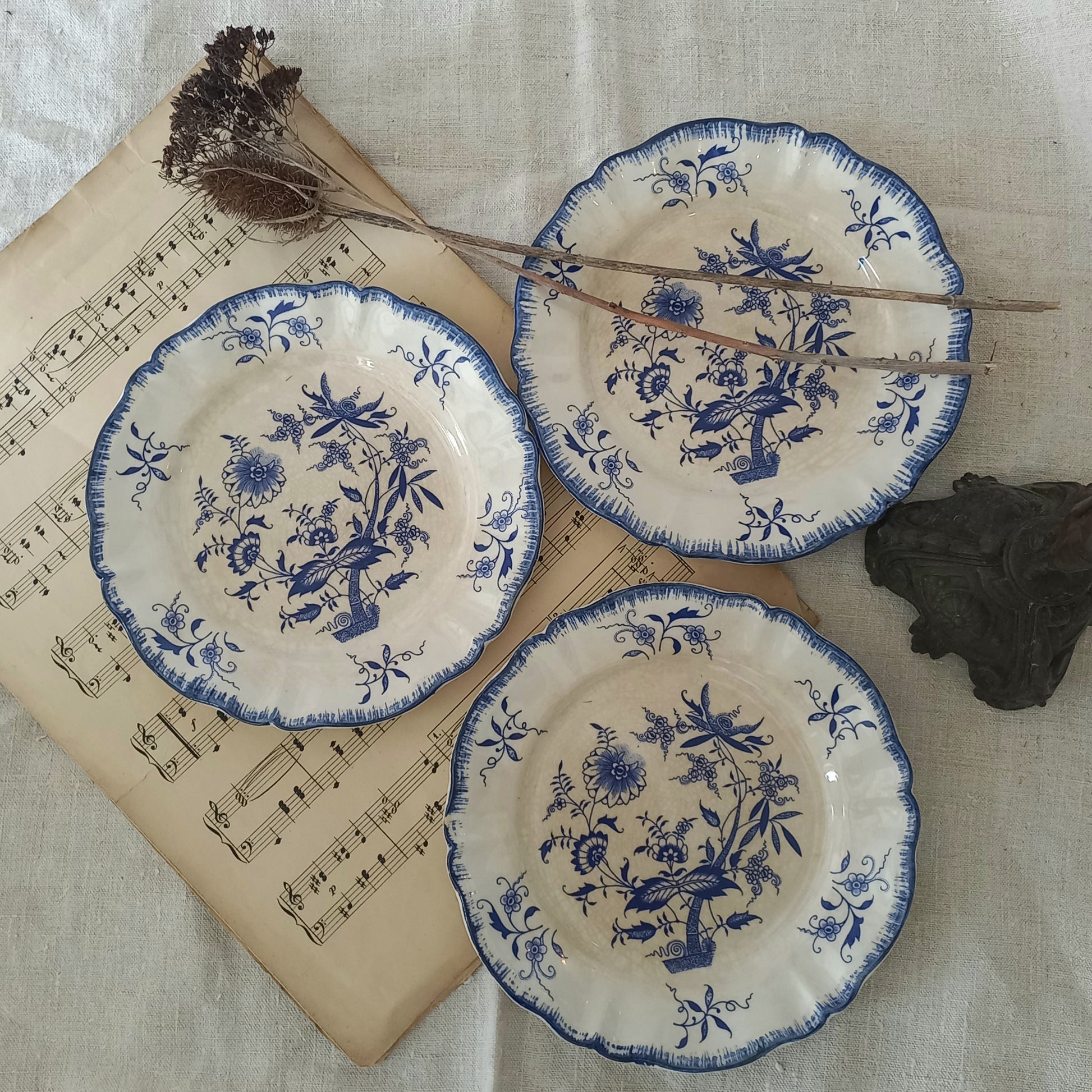 Three ceramic plates with blue floral patterns on a textured surface with music sheet and branches.