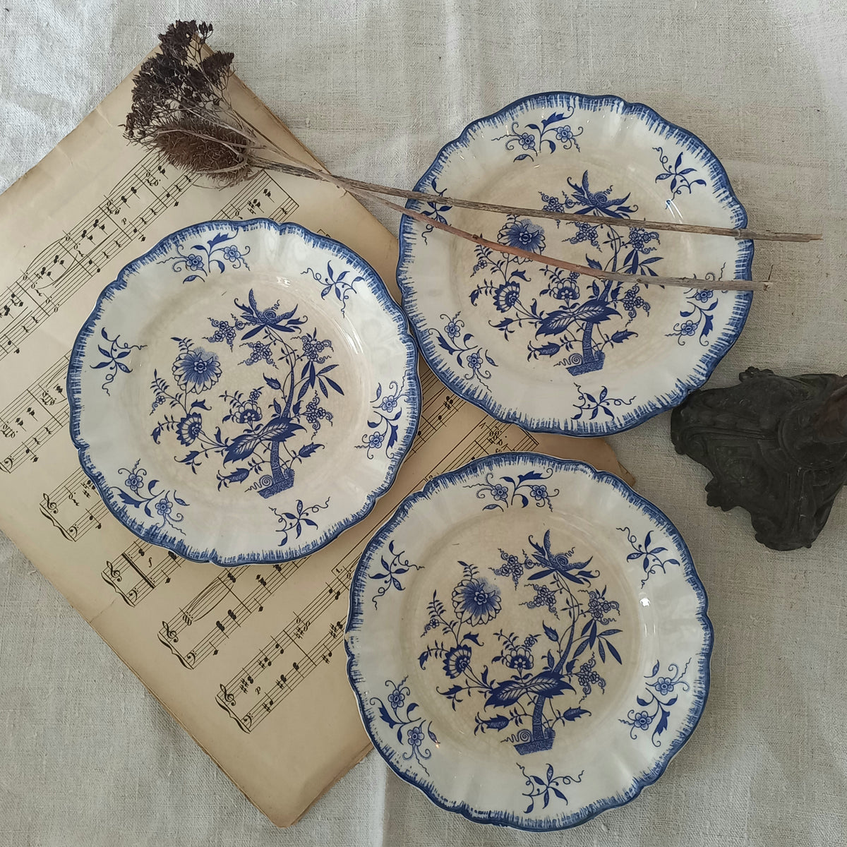Three ceramic plates with blue floral patterns on a textured surface with music sheet and branches.