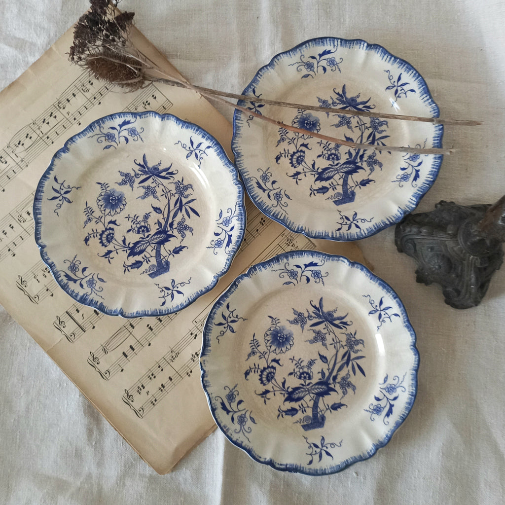 Three blue and white decorative plates on a surface with sheet music and a branch.