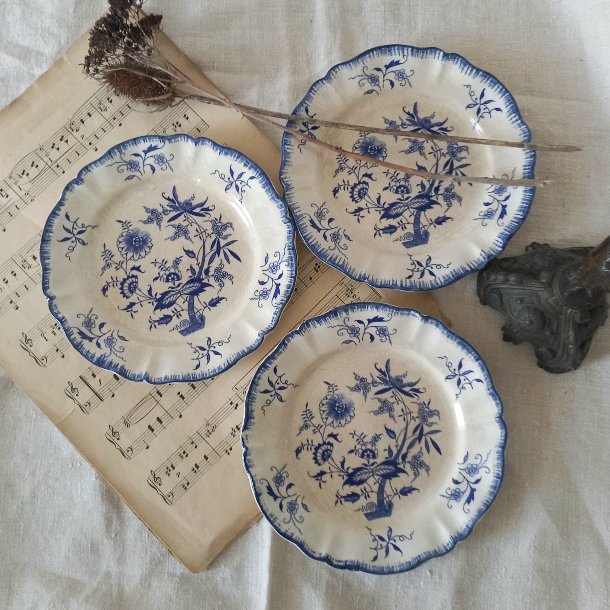Three blue and white decorative plates on a surface with sheet music and a branch.