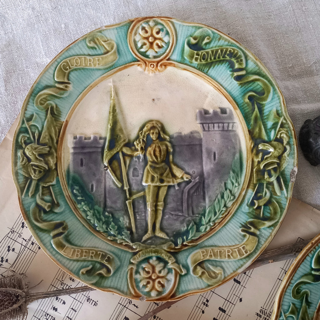 Decorative plate with a central figure holding a spear, surrounded by decorative elements and text.