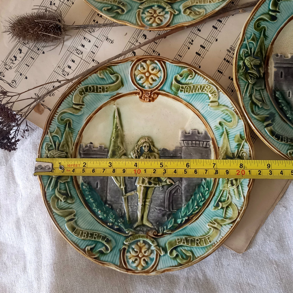 Decorative plate with a Joan of Arc and castle design, measured with a tape measure on a sheet of music.