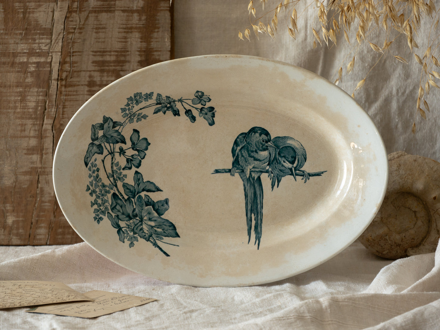 Oval ceramic plate with bird and leaf design on a textured surface