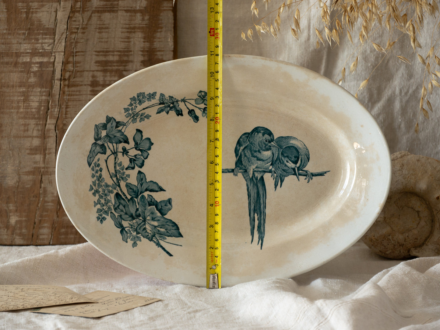 Decorative plate with bird and leaf design, measured by a ruler, on a textured surface.
