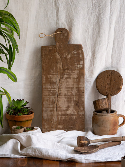 A large vintage wooden chopping board from south west France, shaped by years of use and hand-worn edges. Its rough texture and deep patina tell the story of daily bread, shared meals, and time well lived.