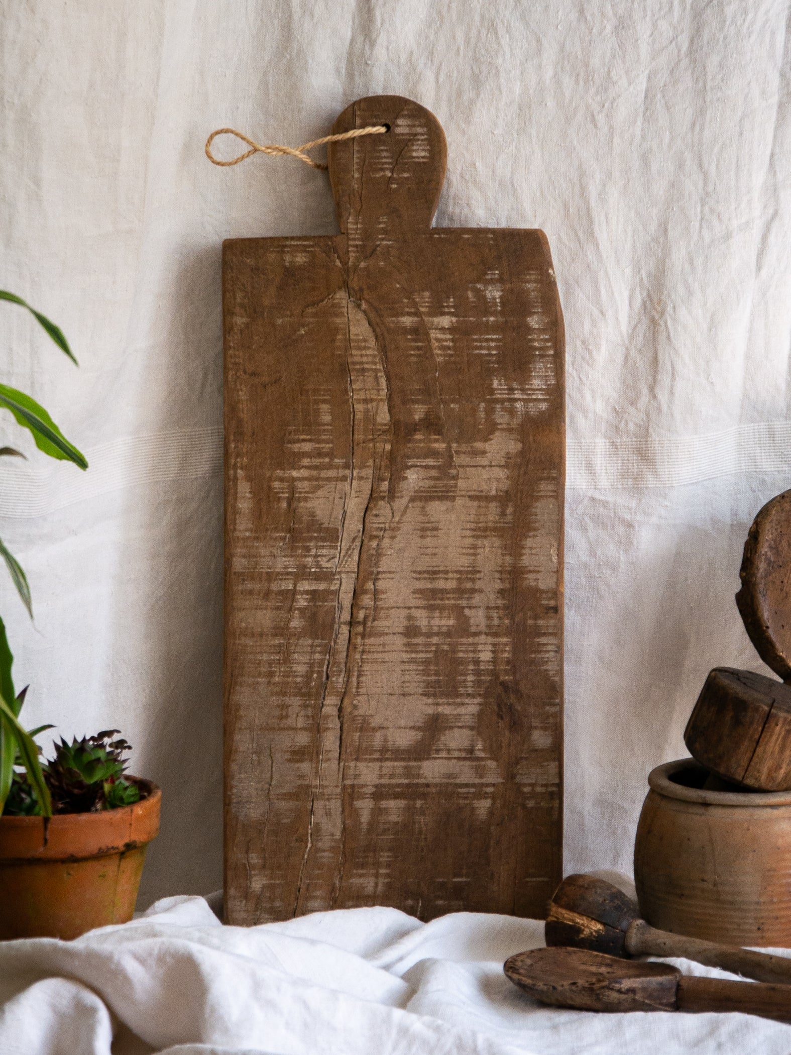 A large vintage wooden chopping board from south west France, shaped by years of use and hand-worn edges. Its rough texture and deep patina tell the story of daily bread, shared meals, and time well lived.