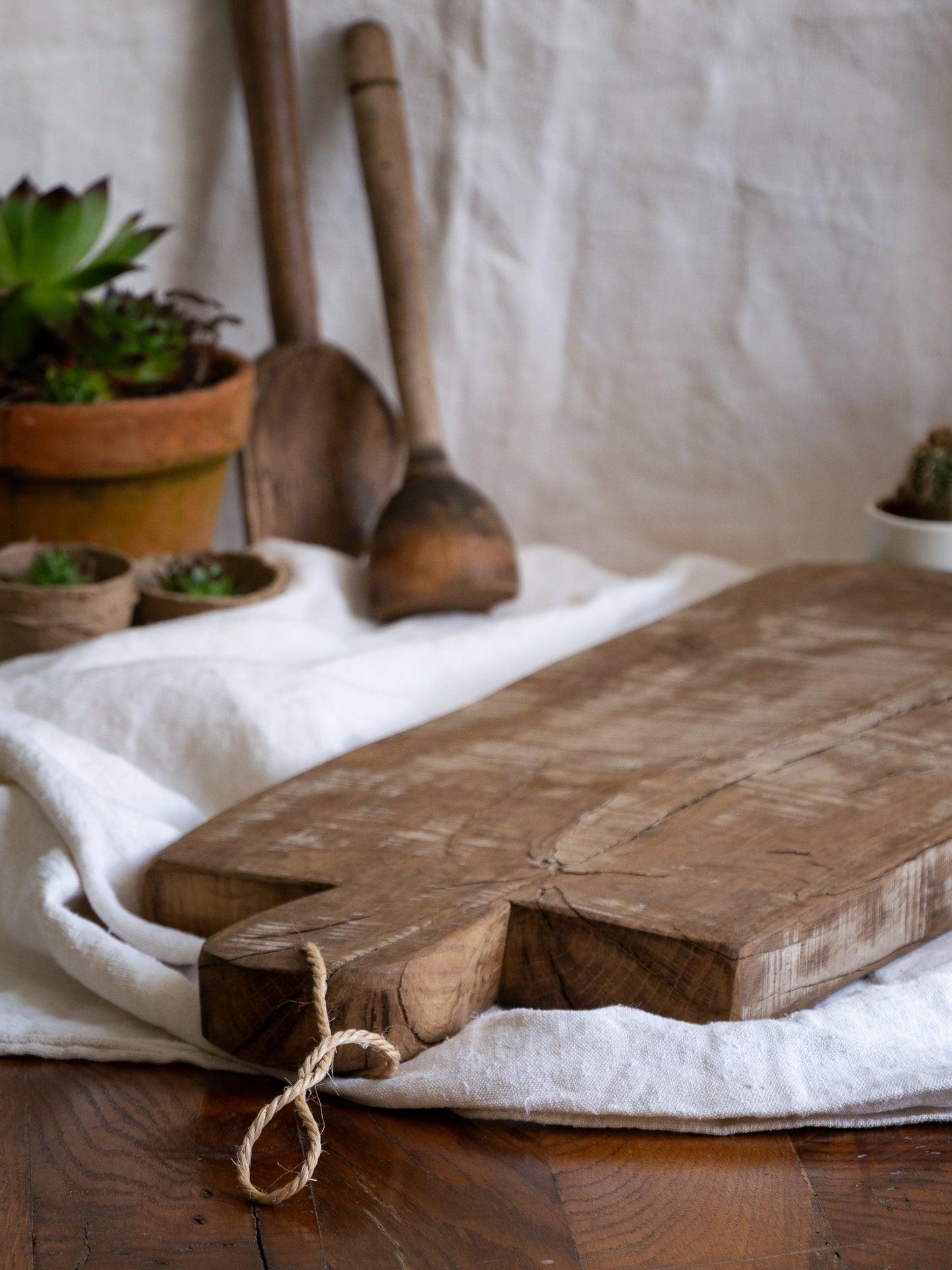 A large vintage wooden chopping board from south west France, shaped by years of use and hand-worn edges. Its rough texture and deep patina tell the story of daily bread, shared meals, and time well lived.