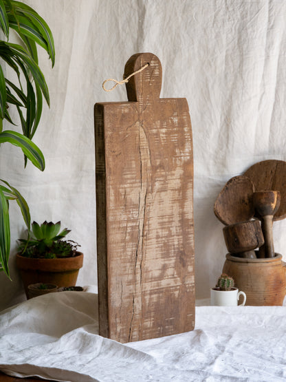 A large vintage wooden chopping board from south west France, shaped by years of use and hand-worn edges. Its rough texture and deep patina tell the story of daily bread, shared meals, and time well lived.