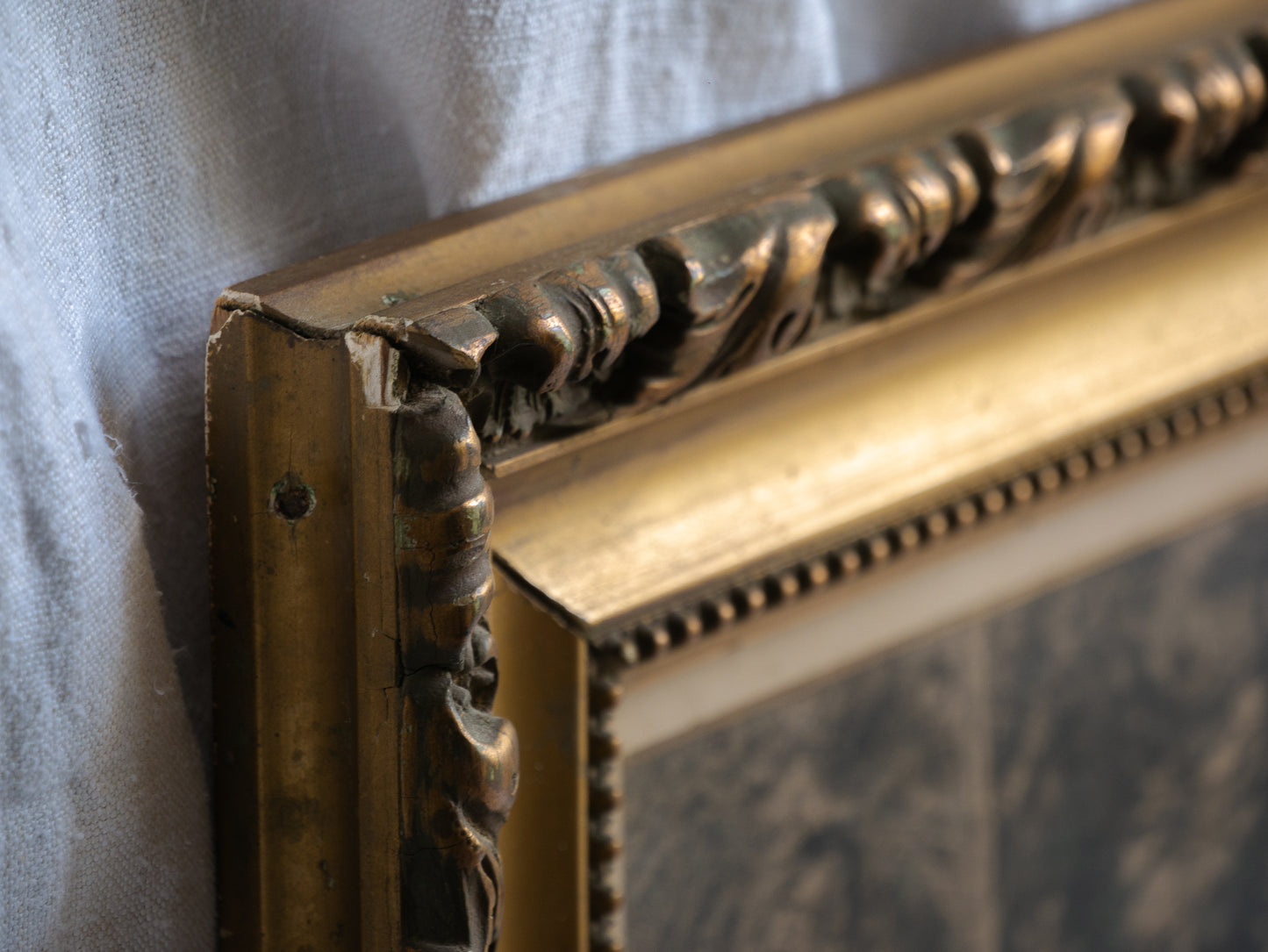 Close-up of an ornate gold picture frame corner on a textured surface.