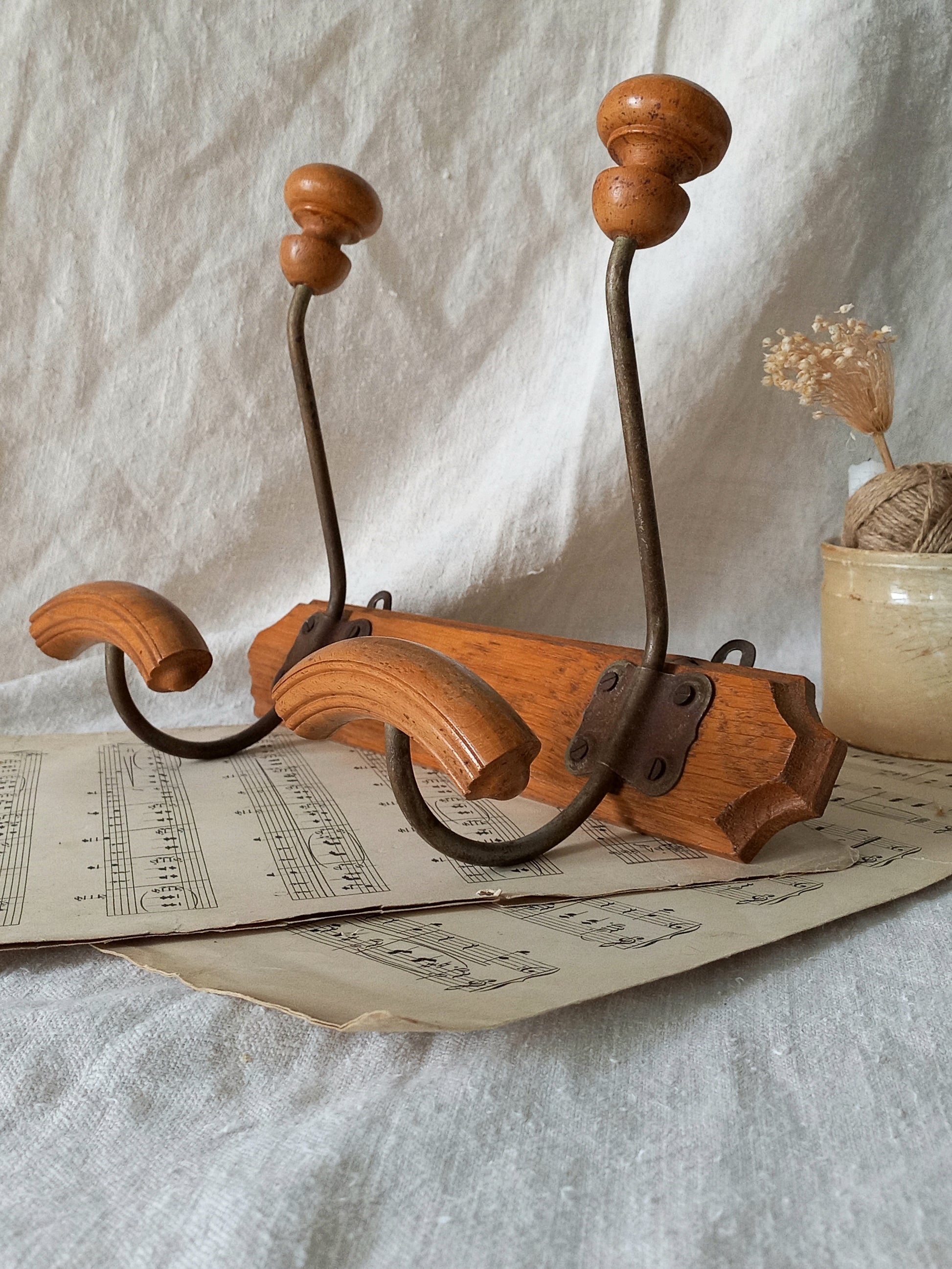 Wooden and metal coat and hat rack on a textured surface with a vase and dried plants in the background