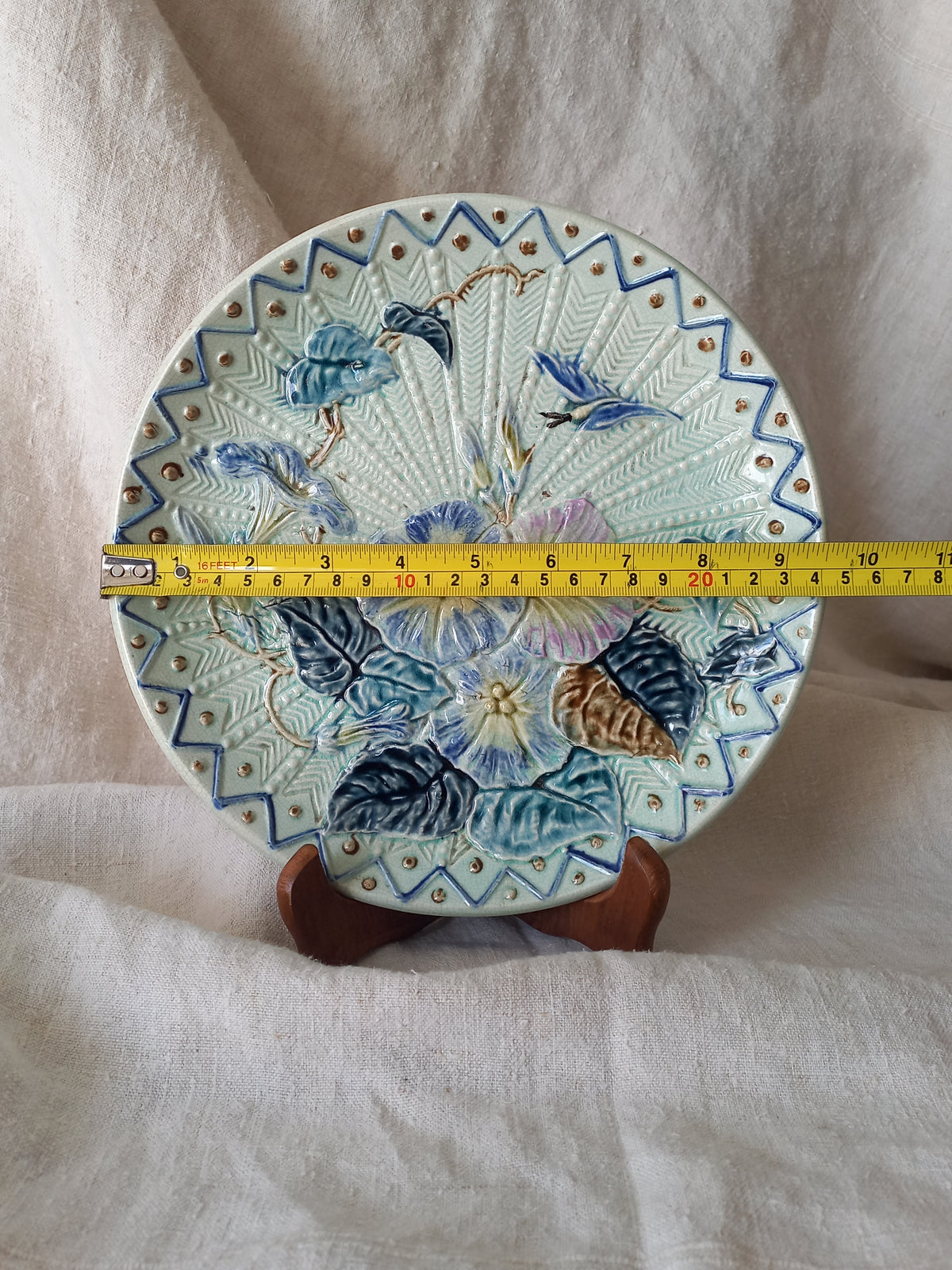 Antique Wasmuel blue floral majolica plate with designs in relief with yellow tape measure for reference.