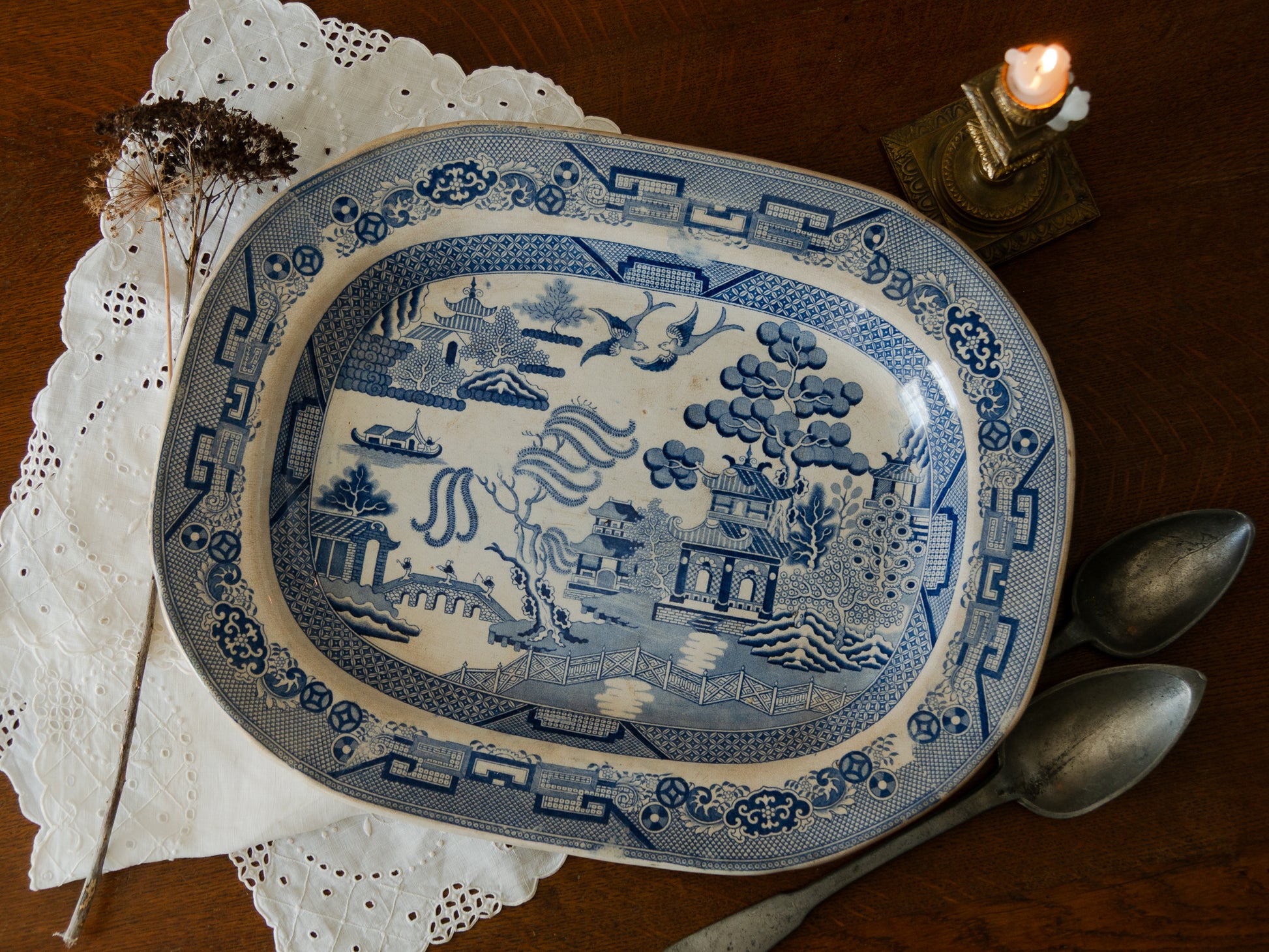 Blue and white patterned plate on a wooden surface with a candle and silverware.