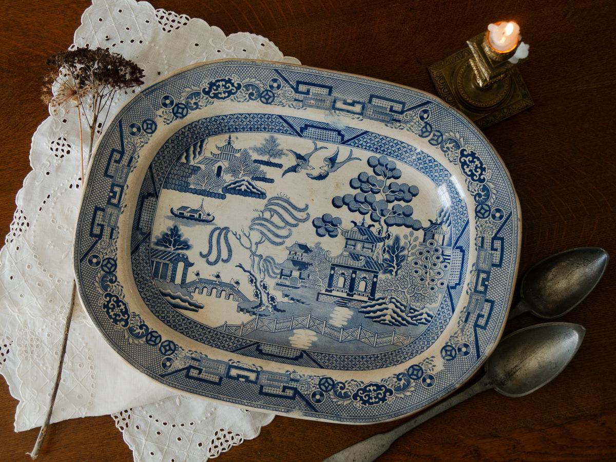 Blue and white patterned plate on a wooden surface with a candle and silverware.