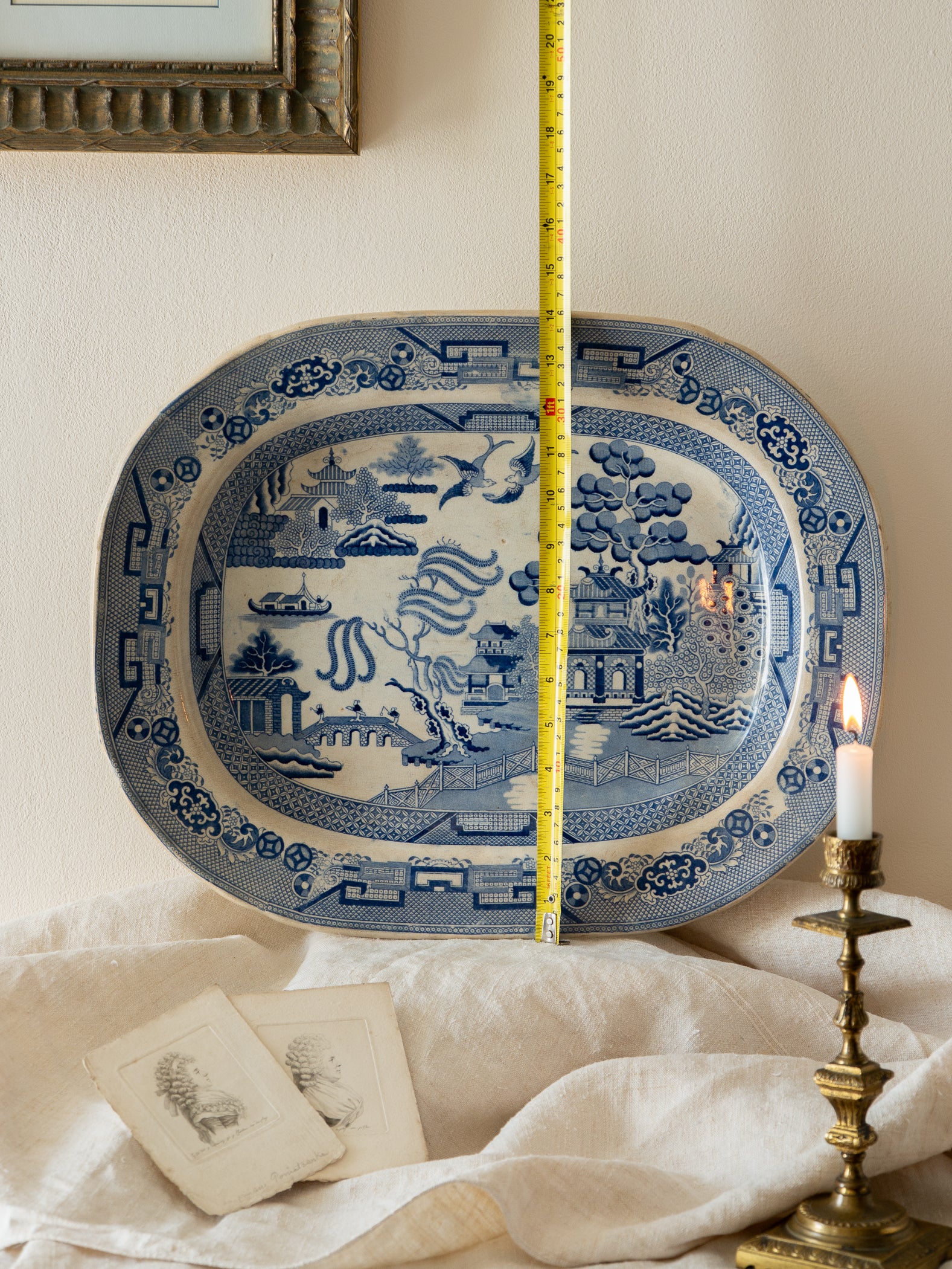 Blue and white decorative plate with a measuring tape, candle, and framed picture in the background.