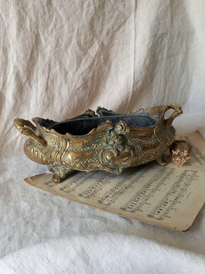 An ornate antique decorative planter resting on a vintage sheet music page against a draped white fabric background.