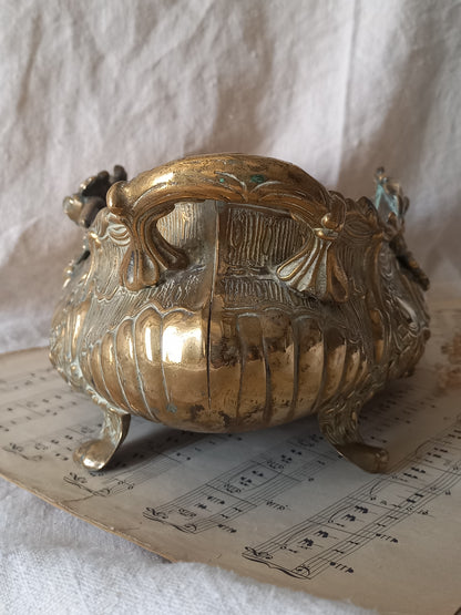 Close-up of an ornate antique decorative planter resting on a vintage sheet music page against a draped white fabric background.