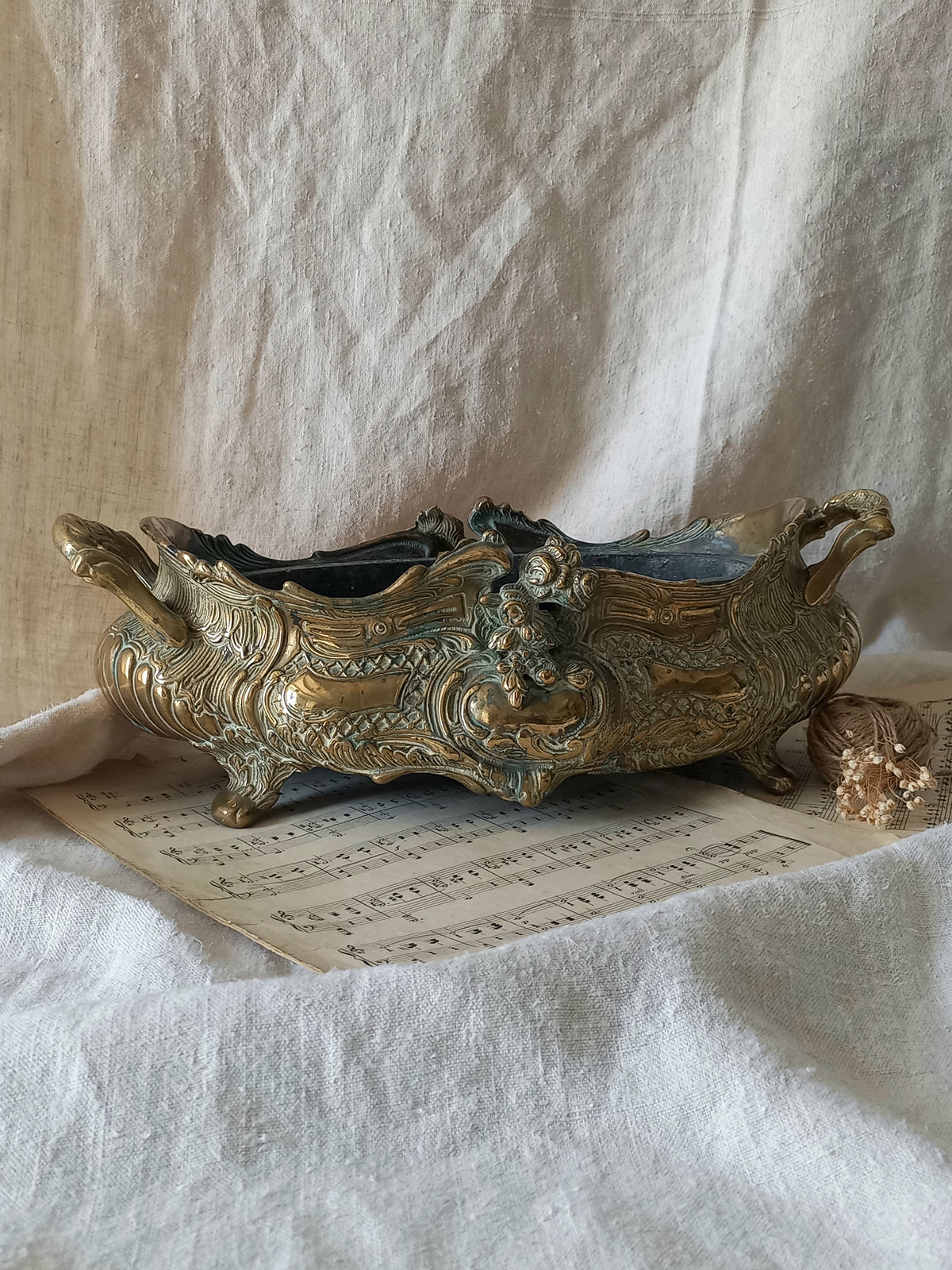 An ornate antique decorative planter resting on a vintage sheet music page against a draped white fabric background.