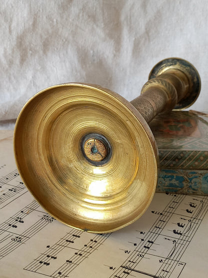 A close-up of the underneath of a brass candle holder, resting on printed sheet music with a textured white fabric background.