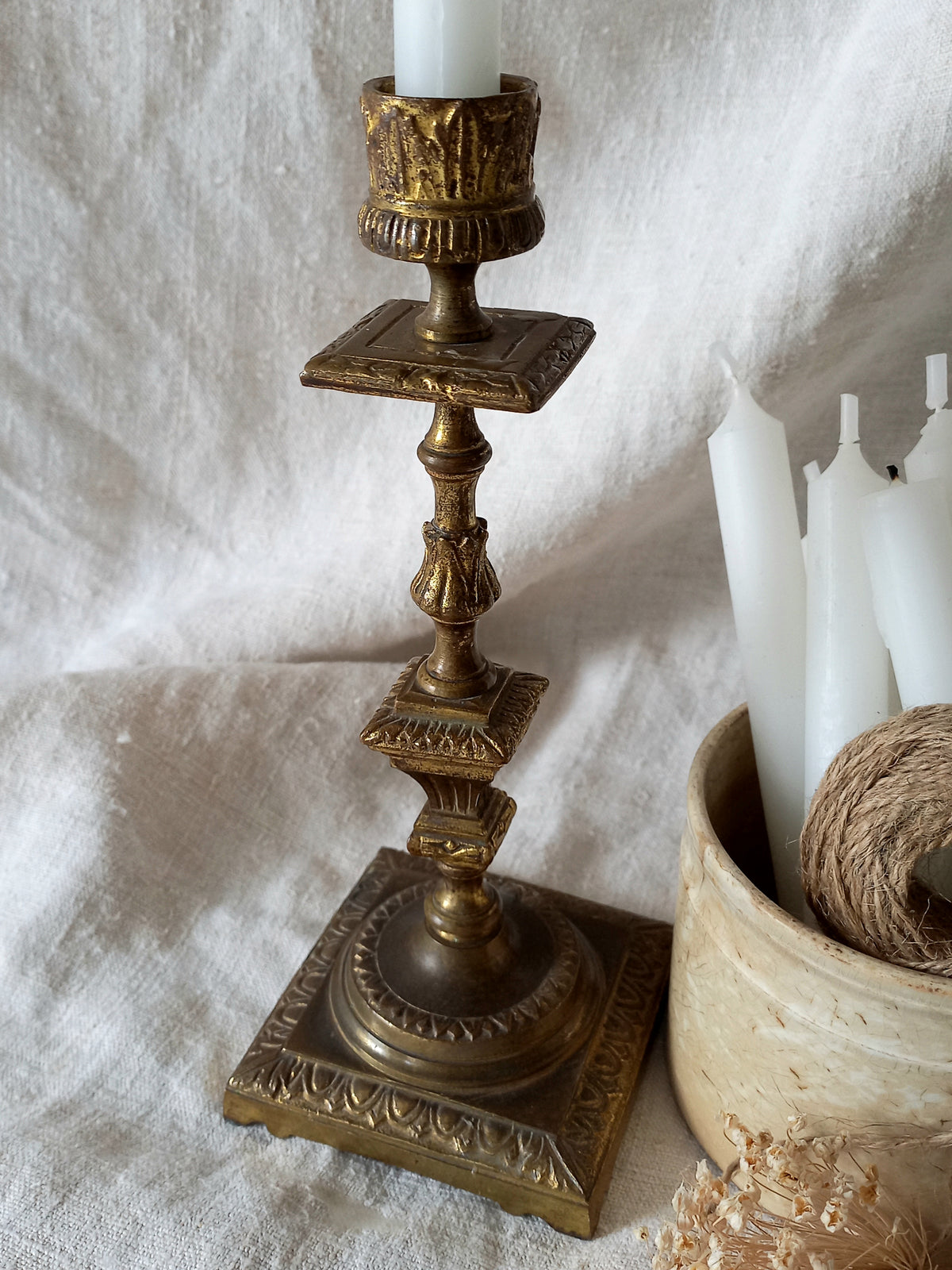Decorative gold candlestick with a white candle on a textured white surface.
