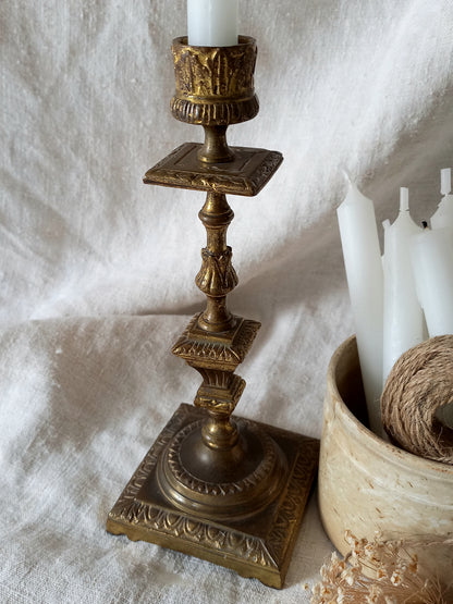 Decorative gold candlestick with a white candle on a textured white surface.