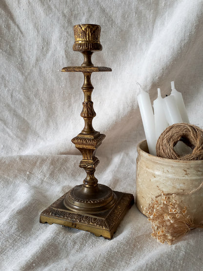 Decorative brass candlestick on a textured white surface with candles and twine.