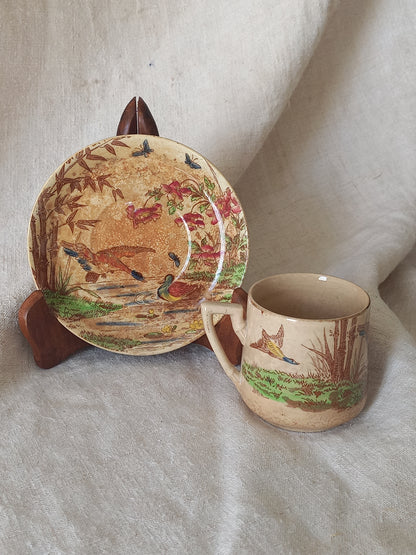 Ceramic cup and saucer with nature-themed design on a light fabric background