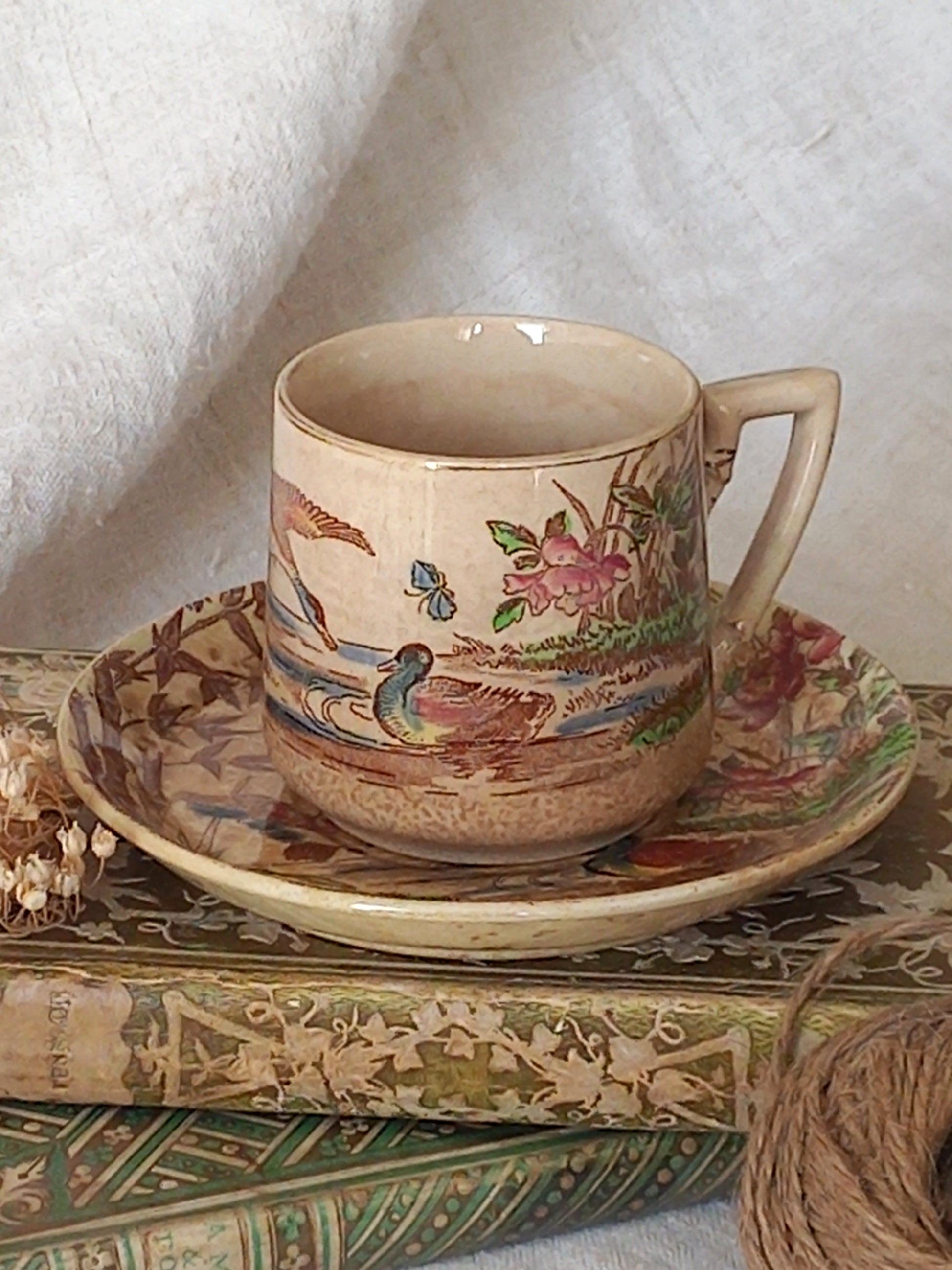 Ceramic cup and saucer with floral and bird patterns on a textured surface.