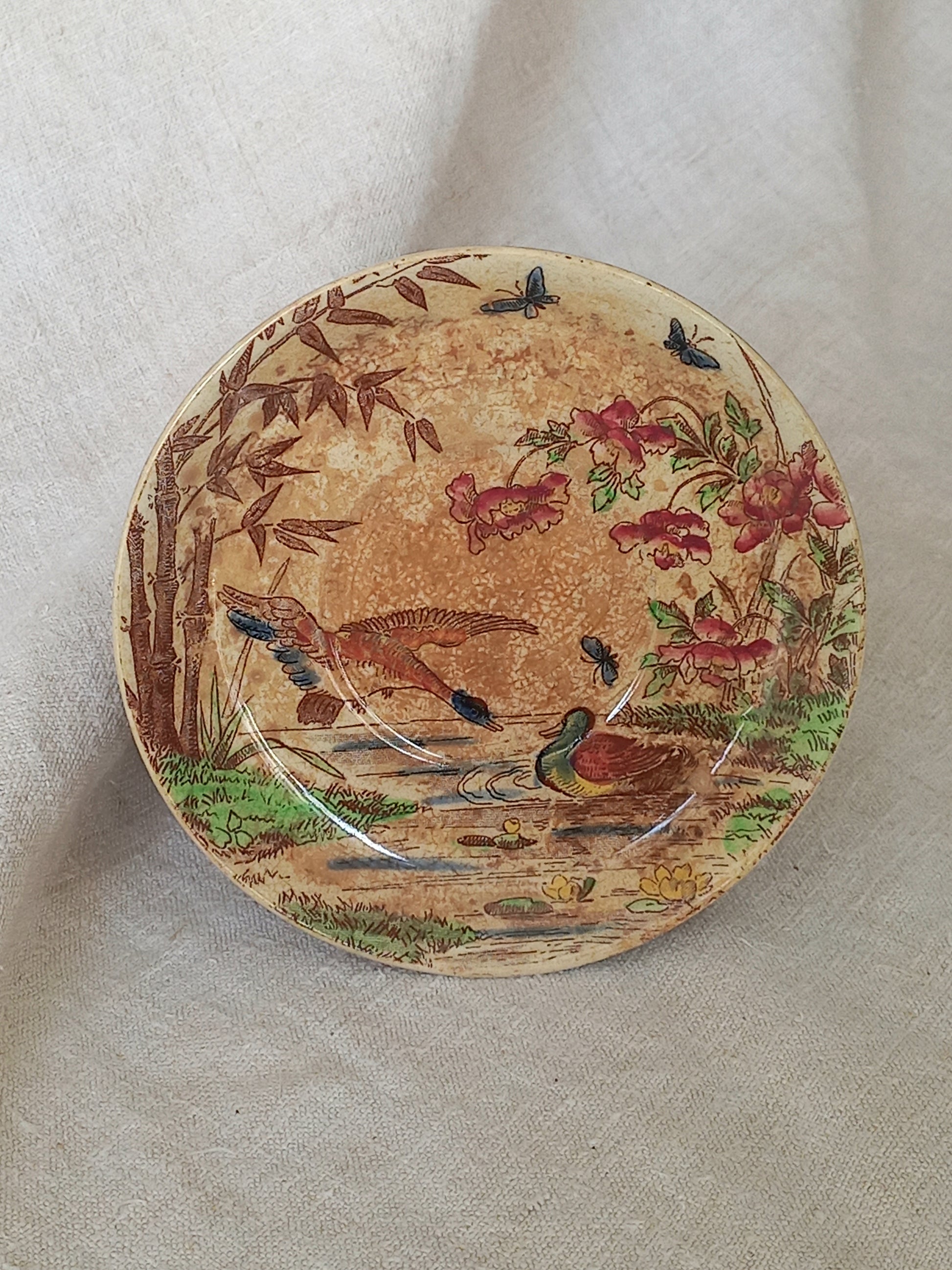 A little antique saucer with oriental influenced design depicting ducks, butterflies, flowers and bamboo shoots.