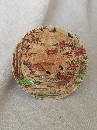 A little antique saucer with oriental influenced design depicting ducks, butterflies, flowers and bamboo shoots.