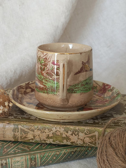 Decorative ceramic cup and saucer with nature-themed design on a textured surface.