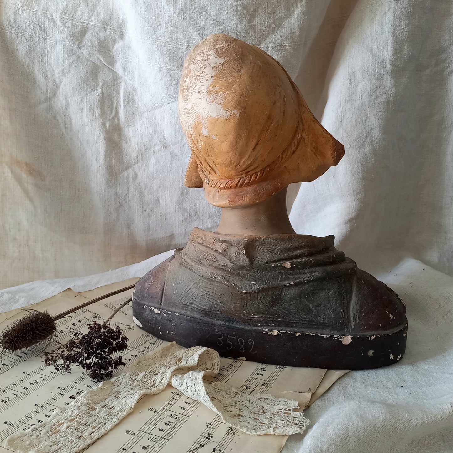 Antique bust of a woman wearing a bonnet on a white fabric background