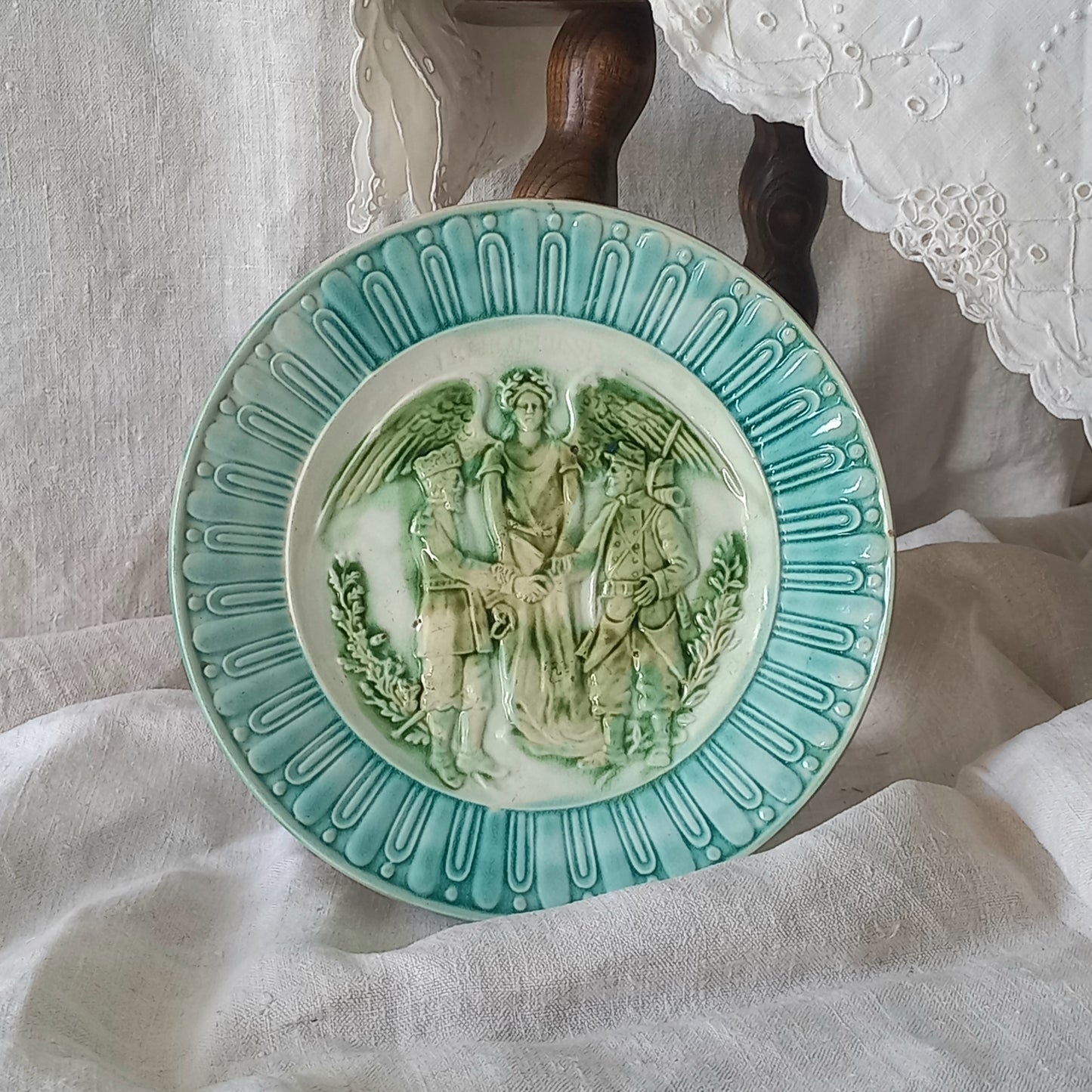 A French antique decorative majolica plate with stunning blue/green colours and an interesting historical background.

This lovely old plate was manufactured as a commemorative piece to celebrate the Franco-Russian Alliance made by the French Republic and the Russian Empire between 1891-1894 (military co-operation agreements) – and that lasted until 1917. The plate depicts a Russian and French soldier shaking hands with a winged female angel in between them.