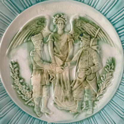 A French antique decorative majolica plate with stunning blue/green colours and an interesting historical background.

This lovely old plate was manufactured as a commemorative piece to celebrate the Franco-Russian Alliance made by the French Republic and the Russian Empire between 1891-1894 (military co-operation agreements) – and that lasted until 1917. The plate depicts a Russian and French soldier shaking hands with a winged female angel in between them.
