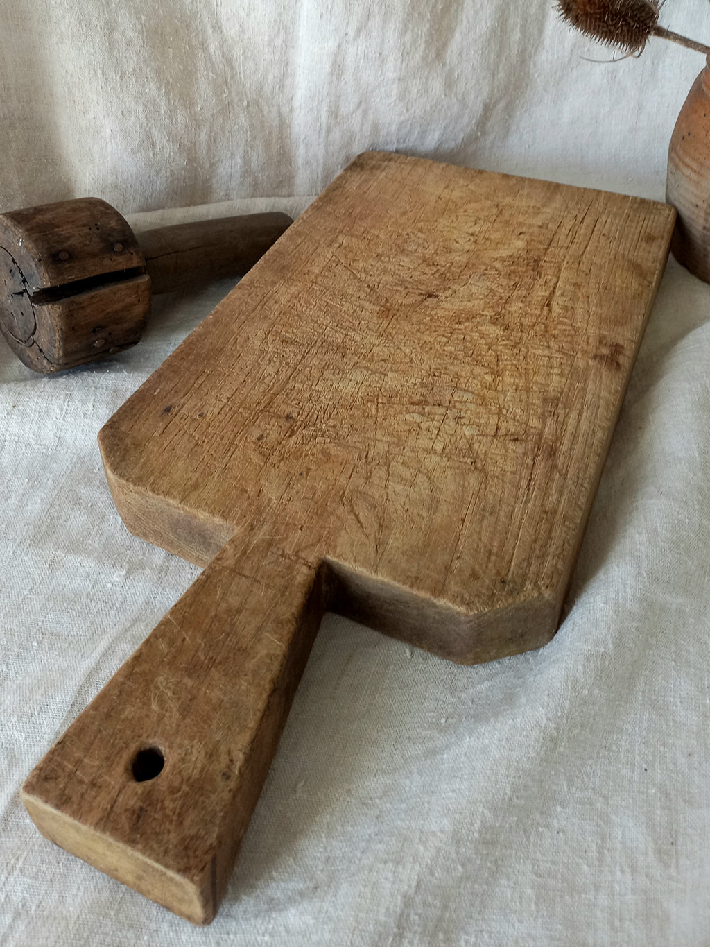 A rustic rectangular wooden cutting board with a handle, resting on a textured off-white linen fabric background.
