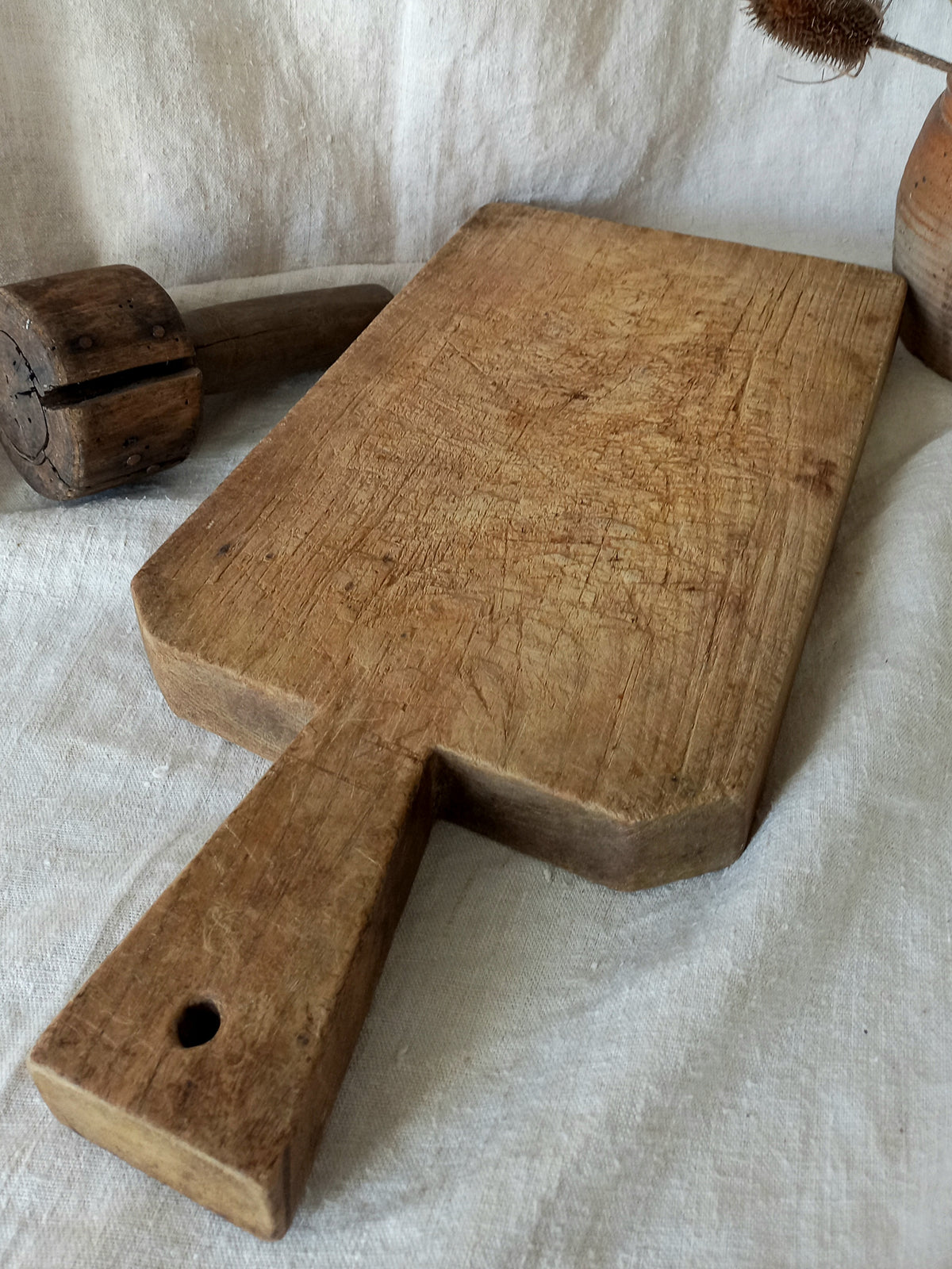 A rustic rectangular wooden cutting board with a handle, resting on a textured off-white linen fabric background.
