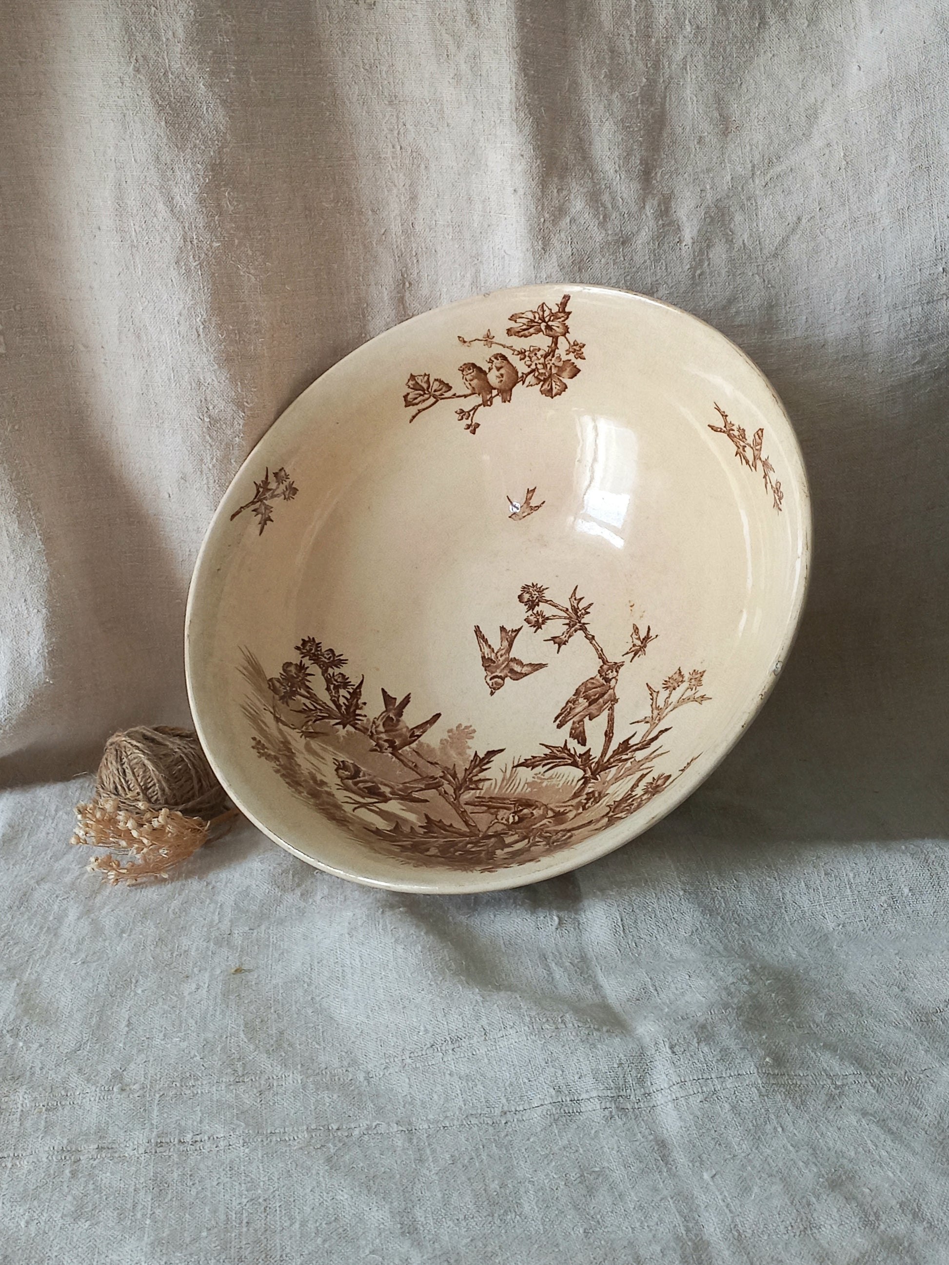 A cream-colored ceramic bowl with a brown sepia floral and bird pattern, resting on a textured light gray linen cloth.