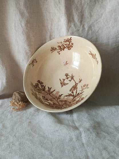 A cream-colored ceramic bowl with a brown sepia floral and bird pattern, resting on a textured light gray linen cloth.