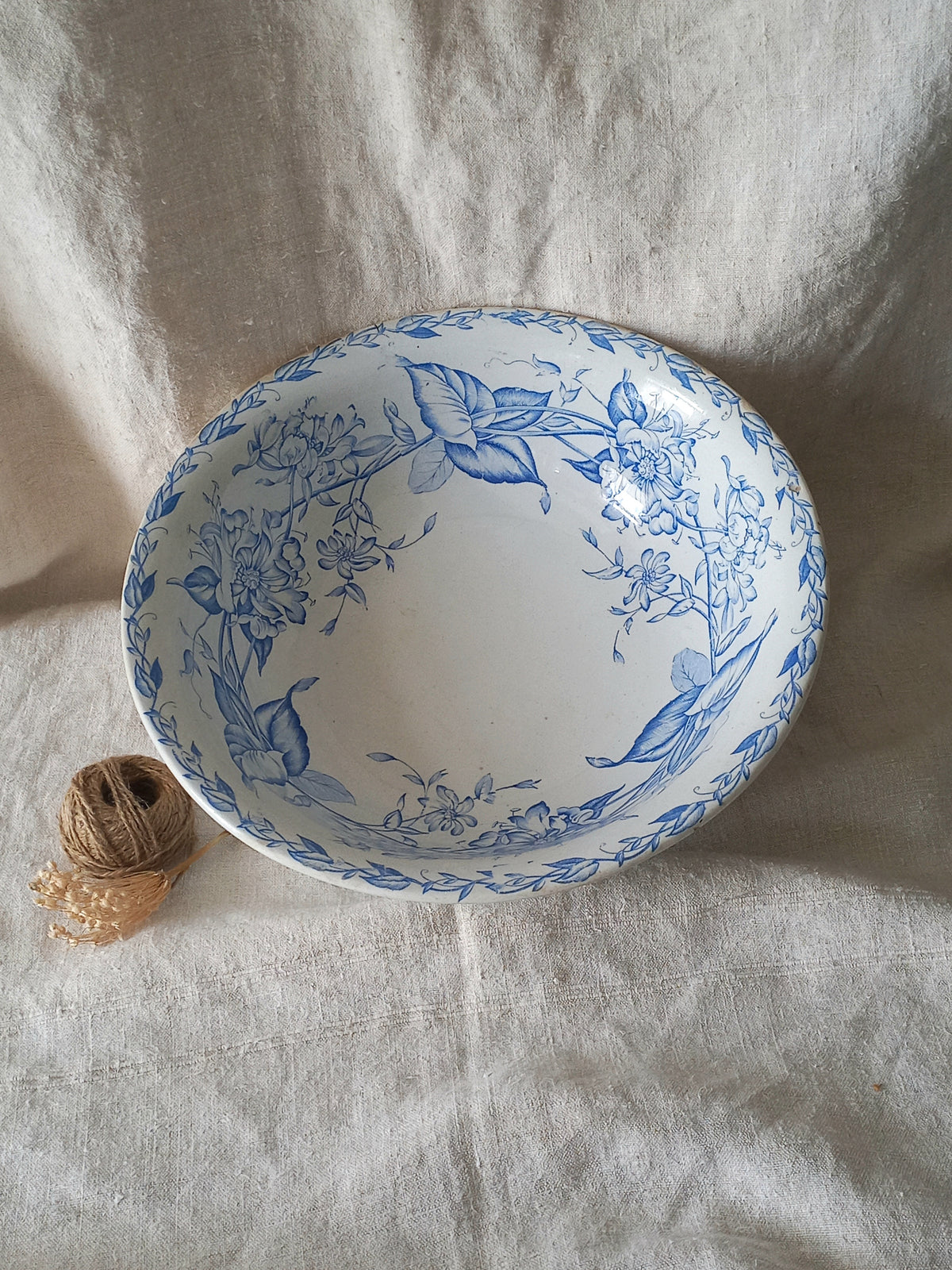 A white ceramic bowl with a blue floral pattern, styled on a textured beige linen cloth next to a small spool of twine.