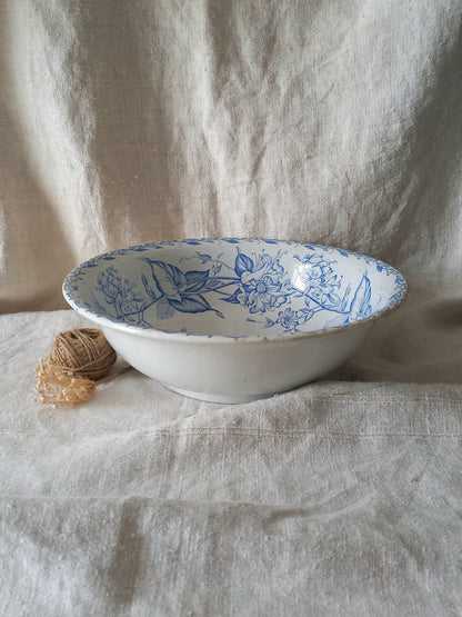 A white ceramic bowl with a blue floral pattern, styled on a draped beige linen fabric backdrop next to a small ball of twine.