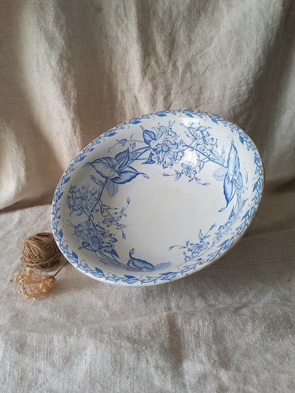 A white ceramic bowl with a blue floral pattern, displayed on a textured beige fabric backdrop next to a small spool of twine.